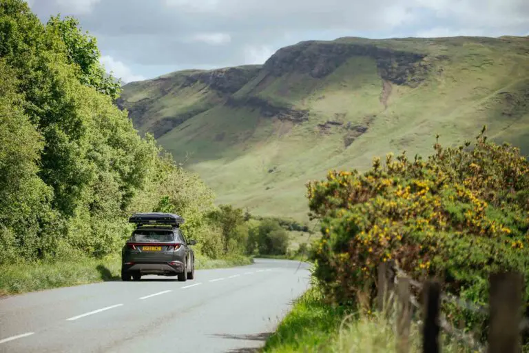 car with roof box driving on a scenic road in Scotland